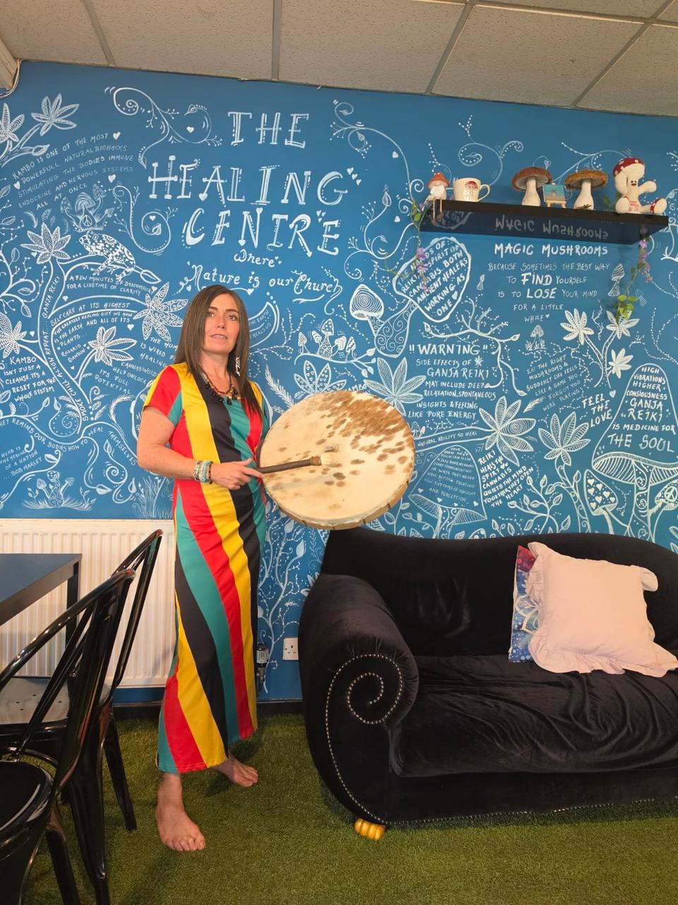 Claire holding a drum by the painted Healing Centre wall
